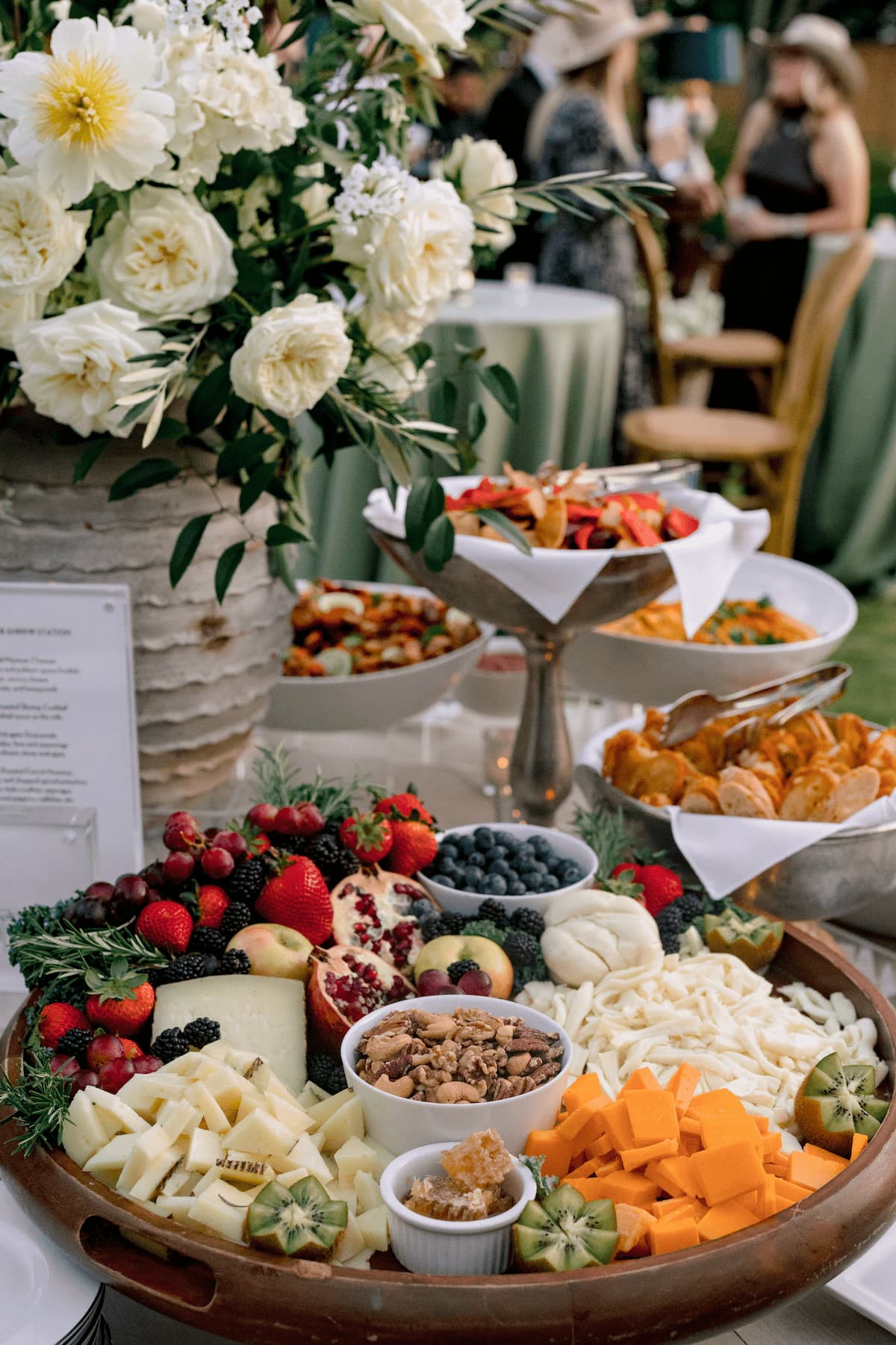 An assortment of cheeses and fruits on a wooden platter.
