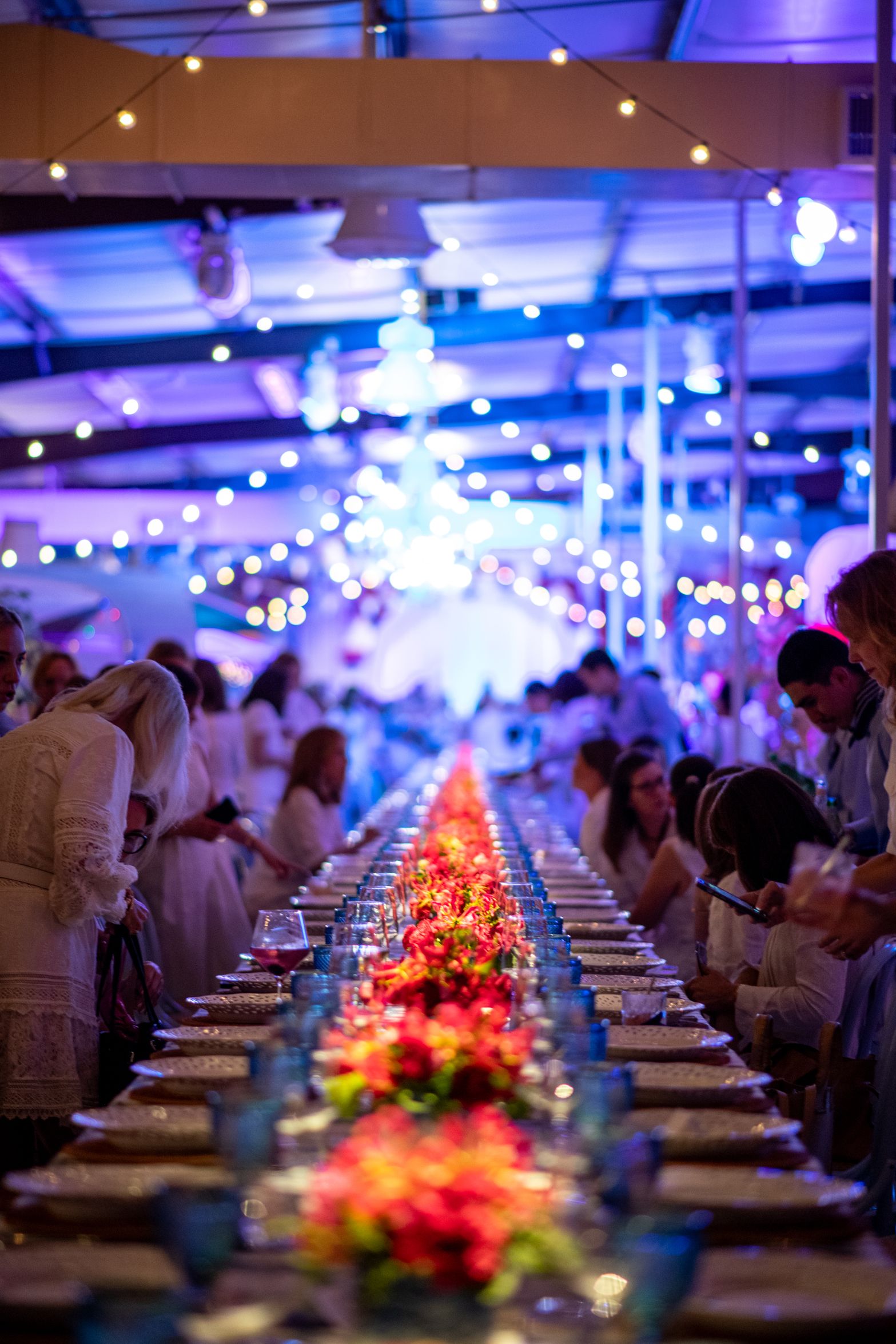 Long dining table adorned with flowers and place settings, illuminated by string lights